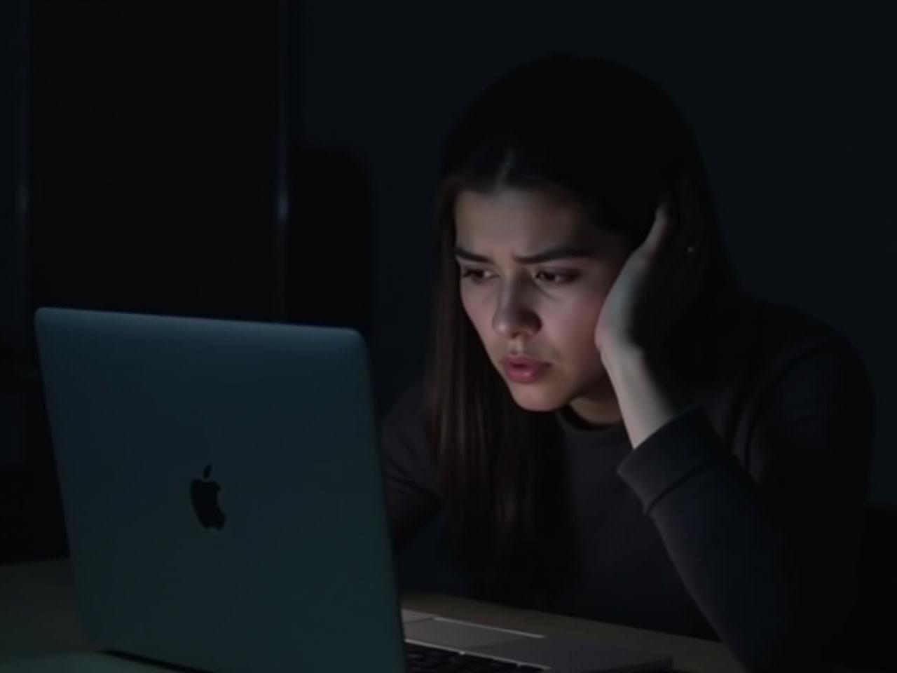 A person looking tired but determined, trying to stay awake while working on a laptop at night.