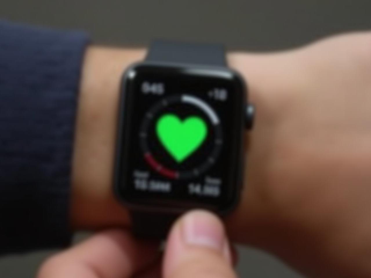 Close-up of a smartwatch displaying Heart Rate Variability data with a green heart symbol. A hand is gently holding the watch.