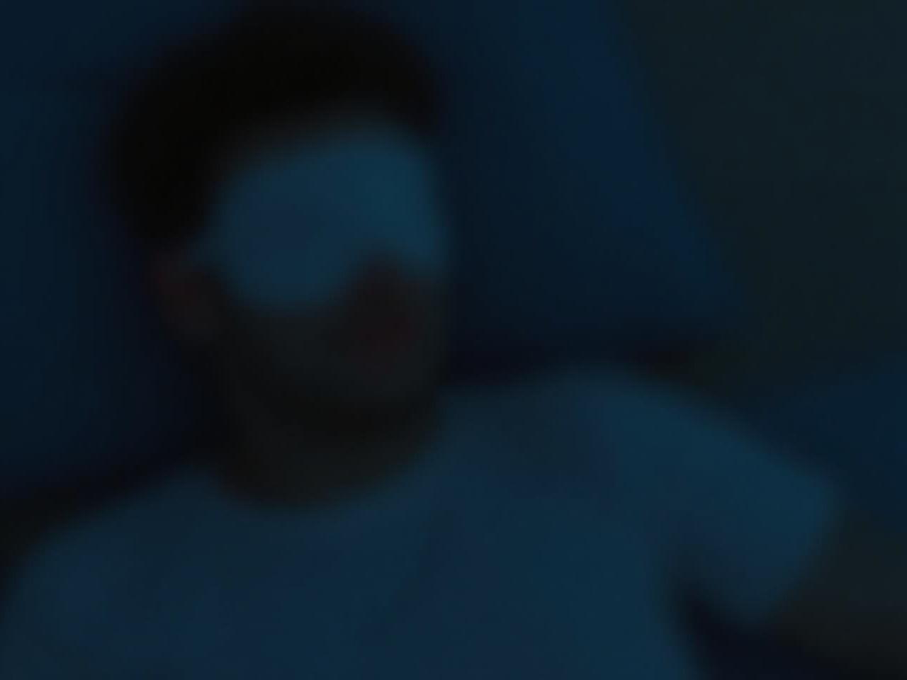 A person wearing a sleep mask in a dimly lit room, symbolizing improved sleep quality.