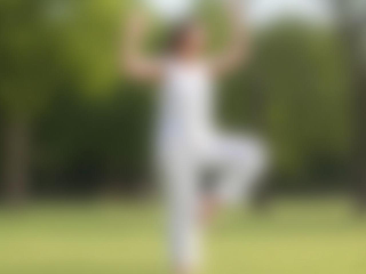 A person gently moving their body in a slow, mindful way, possibly practicing Tai Chi or Yoga, outdoors in a park.